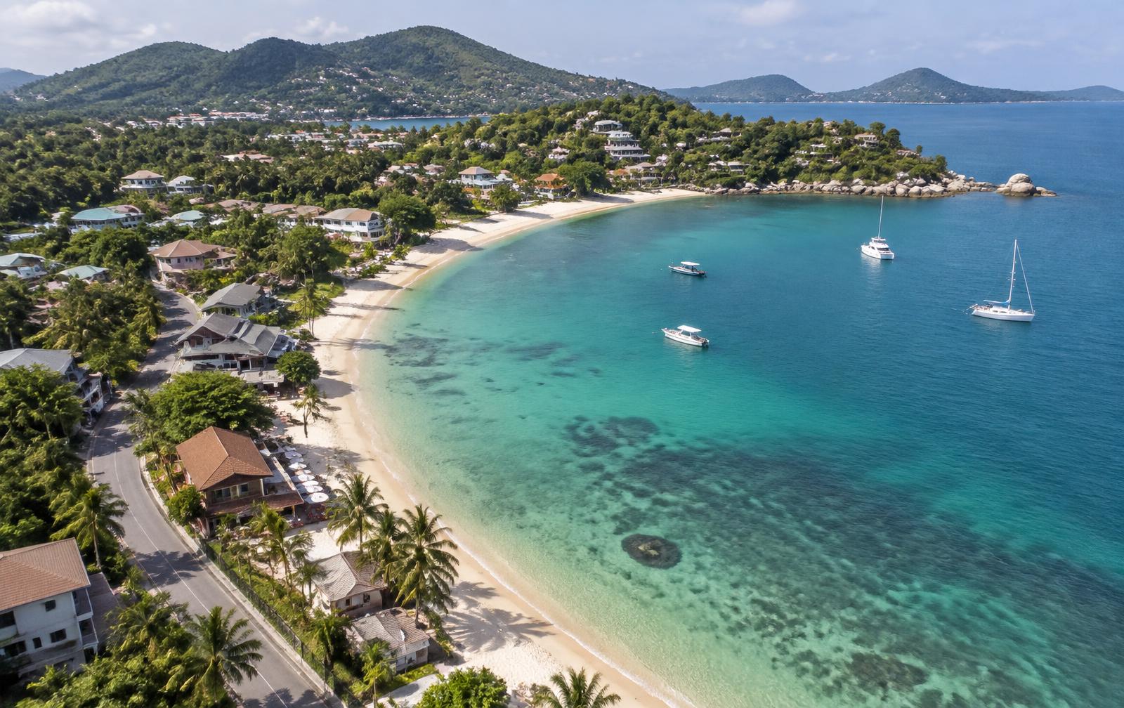Aerial view of Choeng Mon: a calm bay, beach, small restaurants and the coastal road.